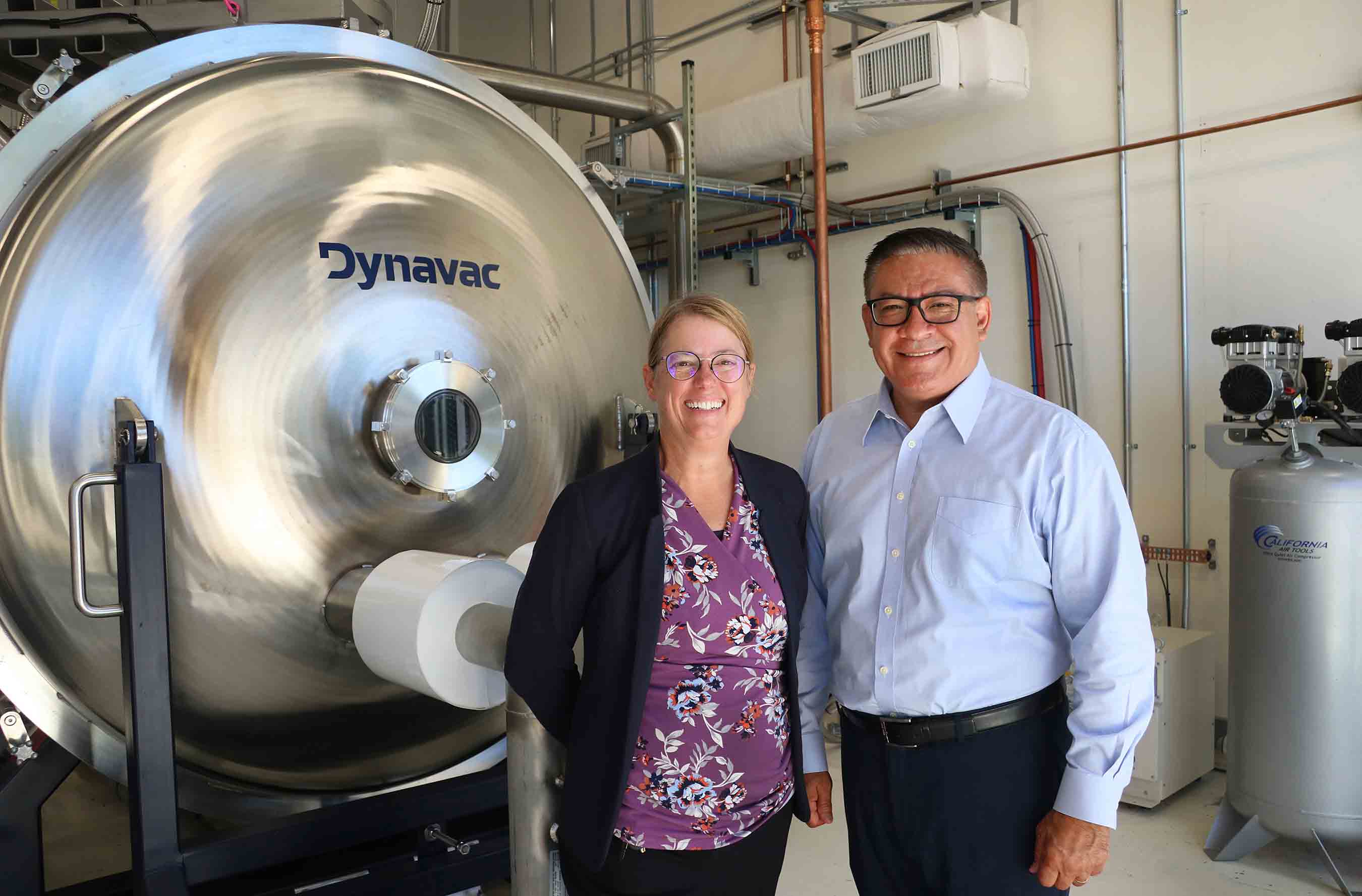 College of Engineering Dean Amy Fleischer and Congressman Salud Carbajal pose in front of a new piece of equipment at the Advanced Technologies Lab.