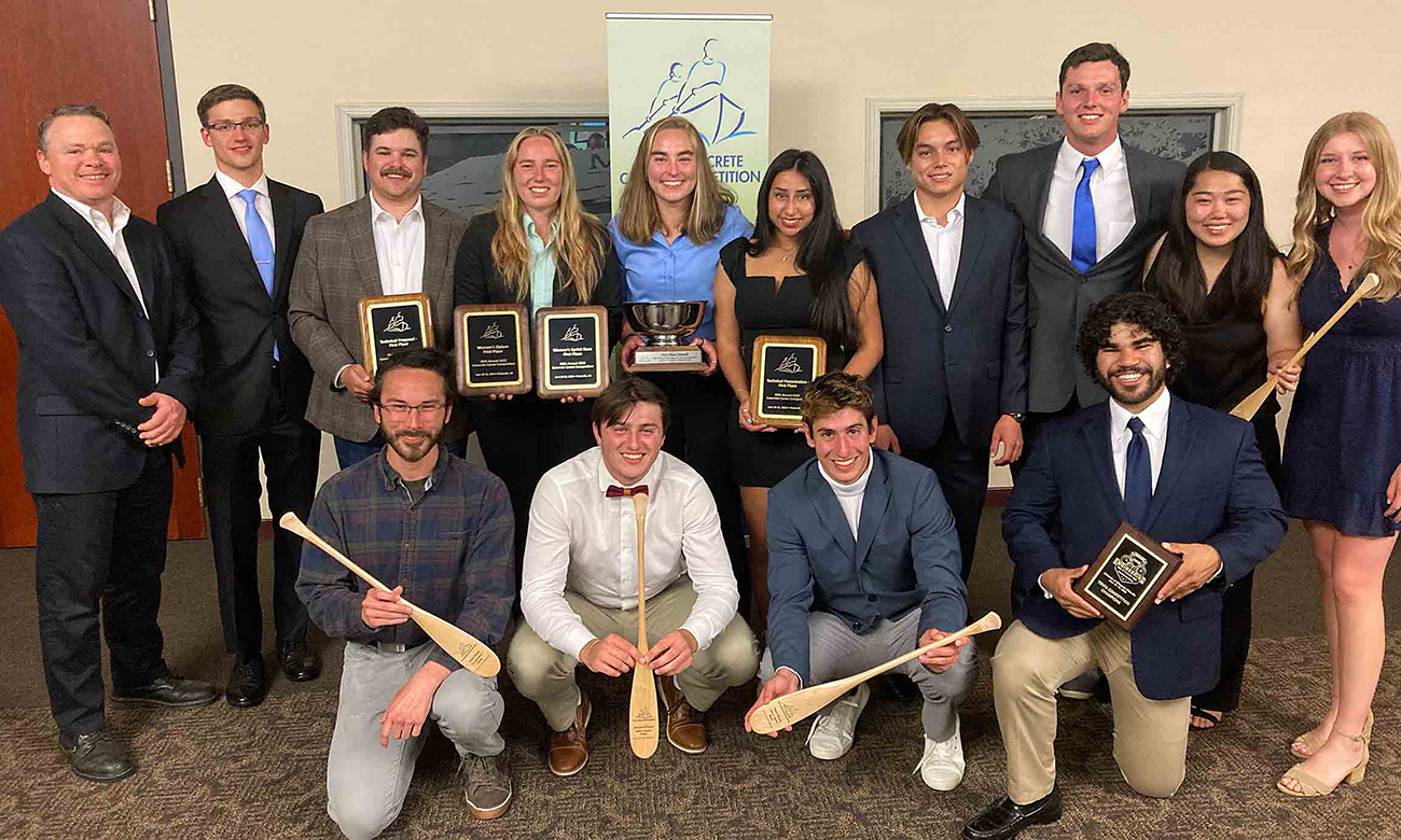 The Cal Poly team and sponsors, in suits and dresses, hold plaques and oar-shaped trophies from the competition.