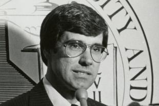 Warren Baker wears glasses while speaking into a microphone 