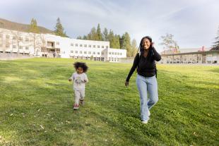 A graduate student and her child run on a field on campus.
