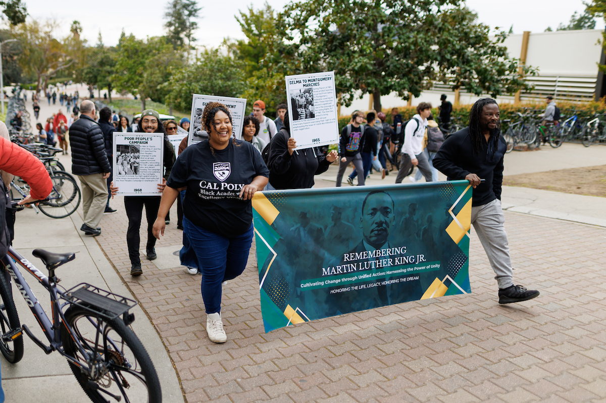 Christina Sholars Ortiz, left, holds up a green and gold banner that says Remembering Martin Luther King Jr. as she marches with students, faculty and staff. 