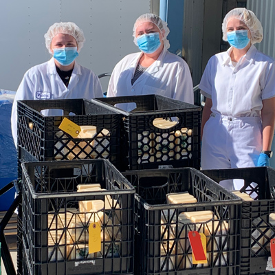 Three people in hairnets and face masks stand behind crates of food. 