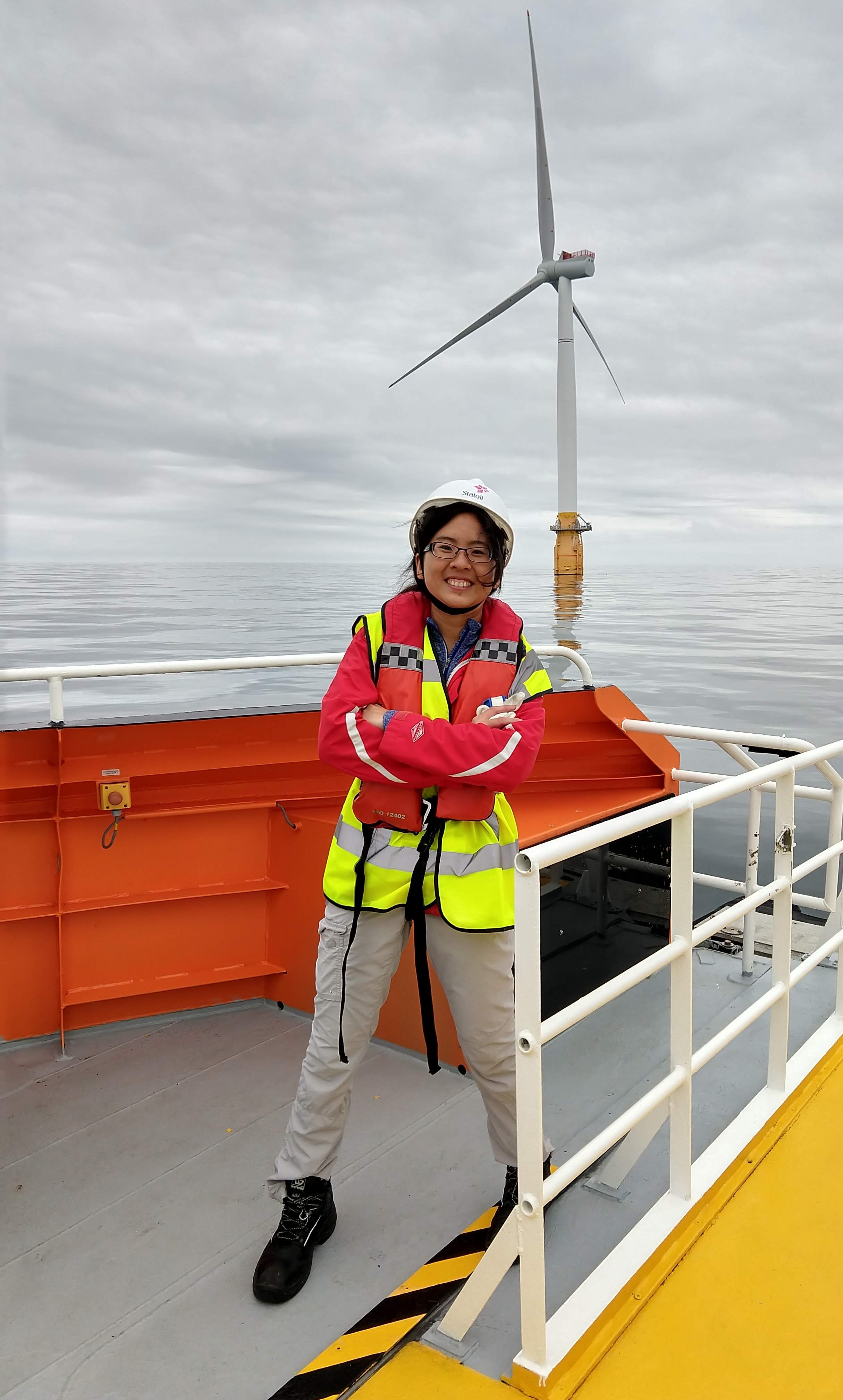 Researcher Yi-Hui Wang, in an orange life vest, on the deck of a boat in front of an offshore wind turbine