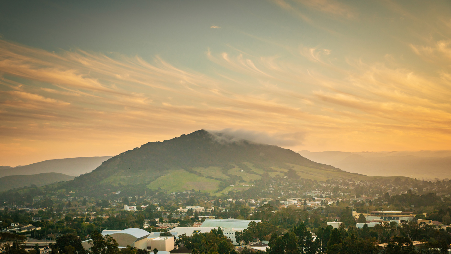 A sunset sky over a mountain with the Cal Poly campus in the foothills