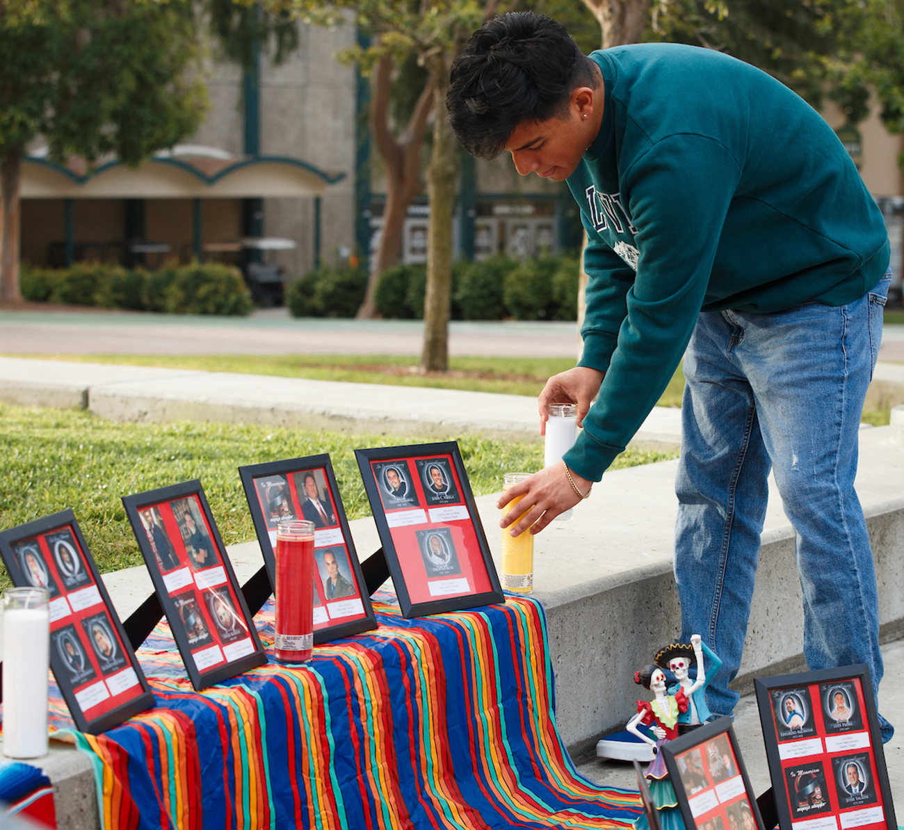 A young man places candles in front of framed photos at an outdoor ofrenda