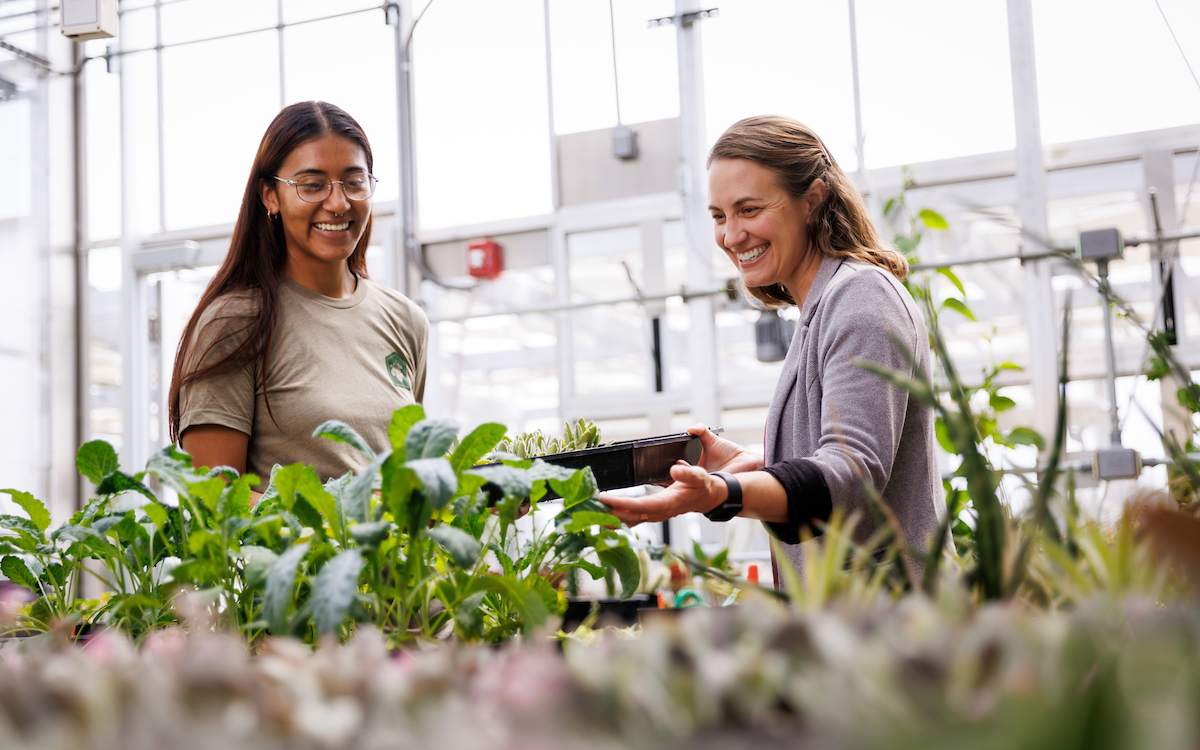 Biological sciences student Monique Alvarez and Jenn Yost share a laugh as they check on a crop of seedlings in the conservatory's research greenhouse. 