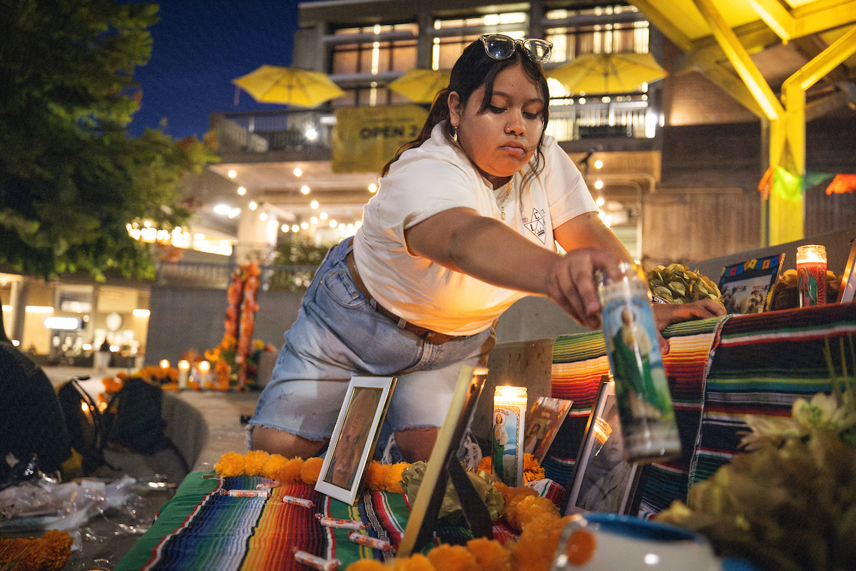 A student places a candle on an ofrenda, or altar, in UU Plaza. Campus community members set up the ofrenda as part of Día de los Muertos in early November.