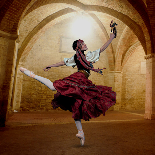 A gypsy dancer in ballet pointe shoes holds a tambourine inside a brick building