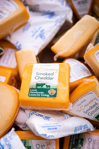A wrapped portion of orange cheddar cheese lays on top of a pile of other cheeses for sale at the Creamery.