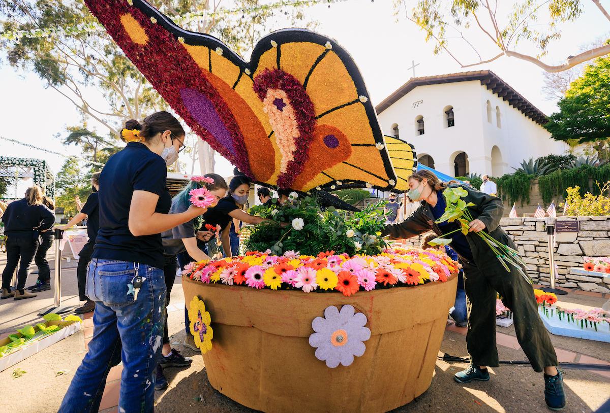 Students surround a flower-covered sculpture of a butterfly rising from flowers at Mission Plaza in San Luis Obispo.