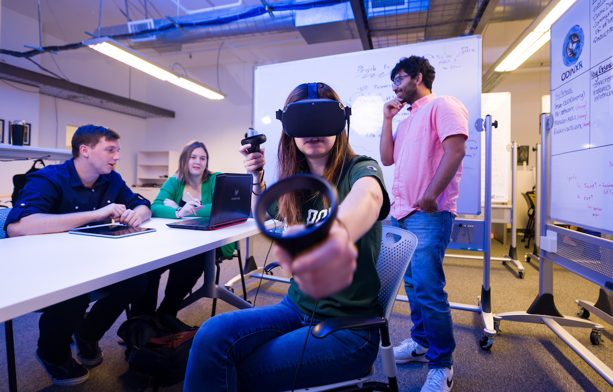 A student wearing VR gear sits at a conference table with other students.