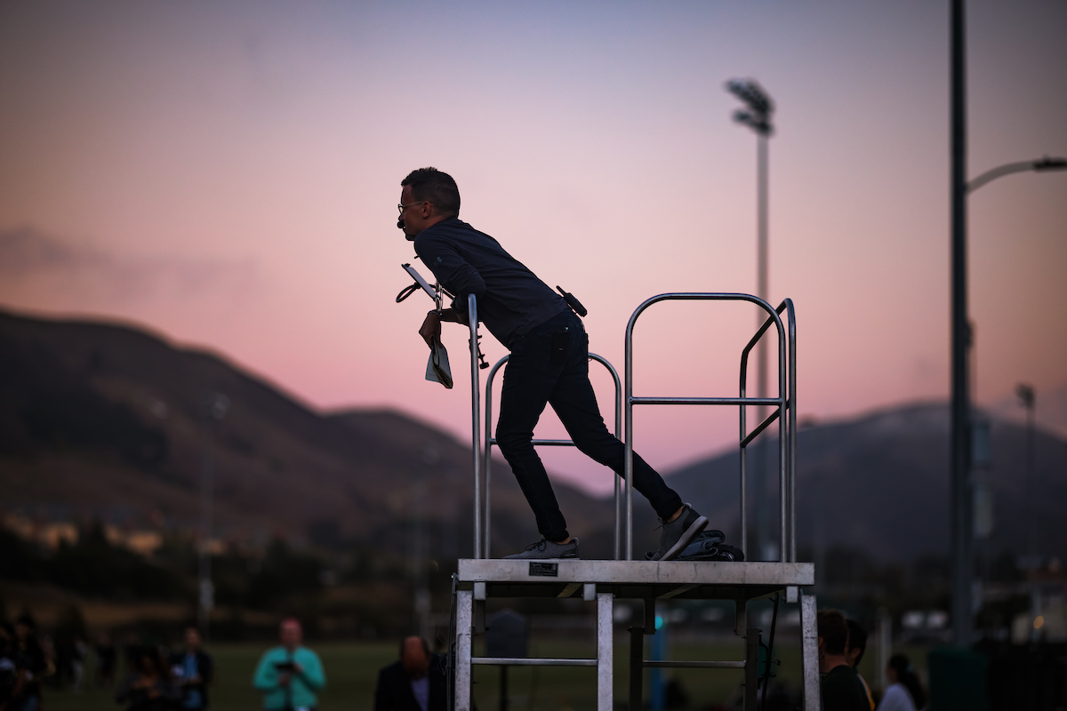 A man leans on a podium, silhouetted against a sunset sky on Cal Poly's campus.