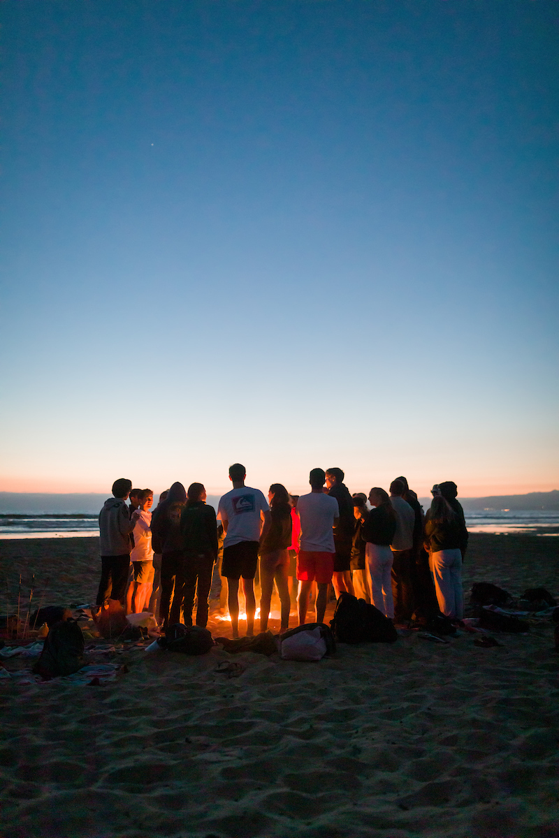 A group of students gathers around a bonfire at Grover Beach during Week of Welcome.