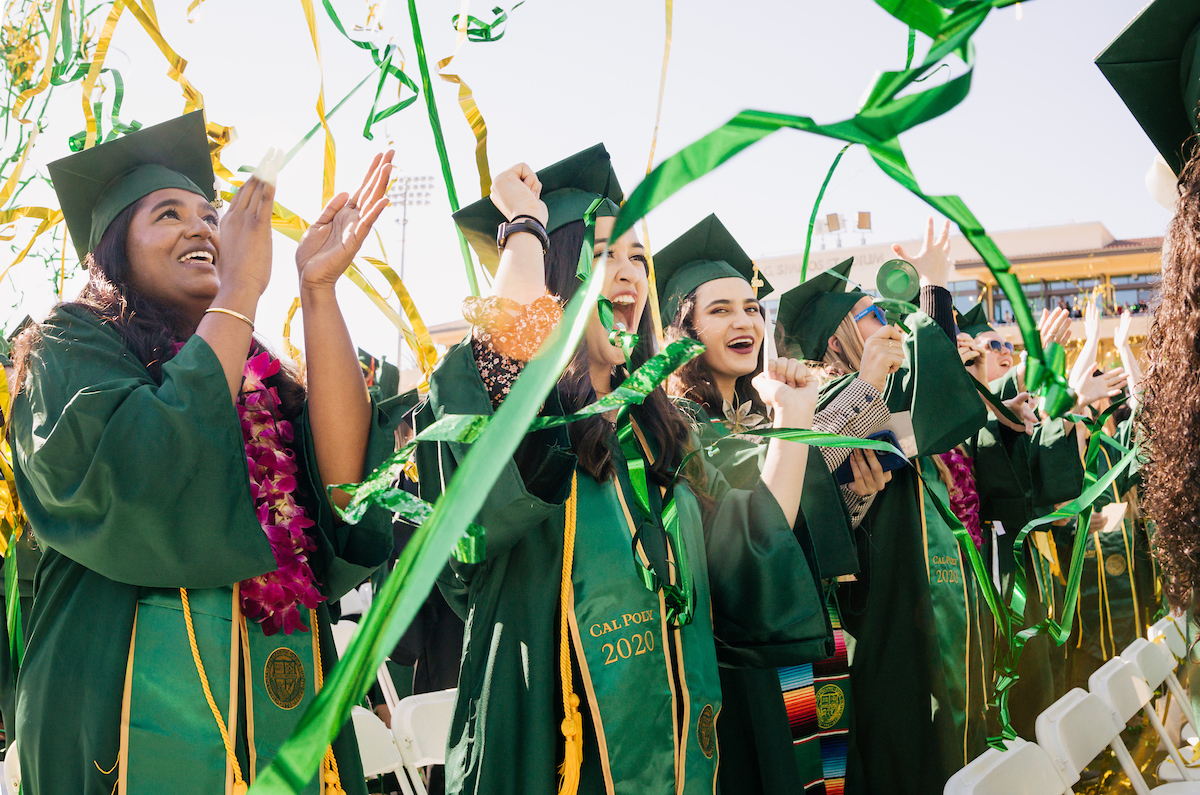 Students wearing green graduation robes cheer as streamers fall around them during graduation. 