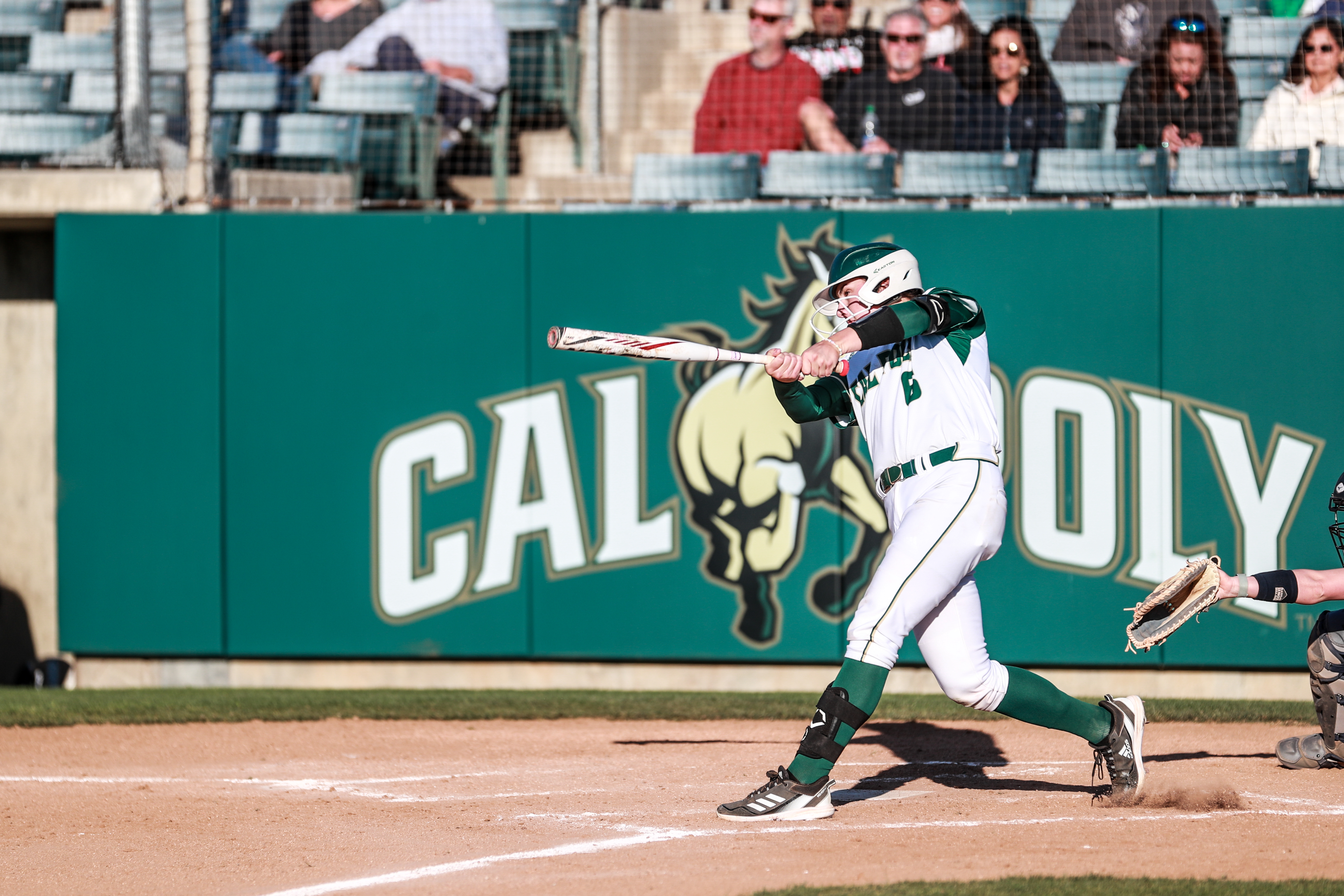 A woman in a white Cal Poly softball uniform bats on the field during a game.