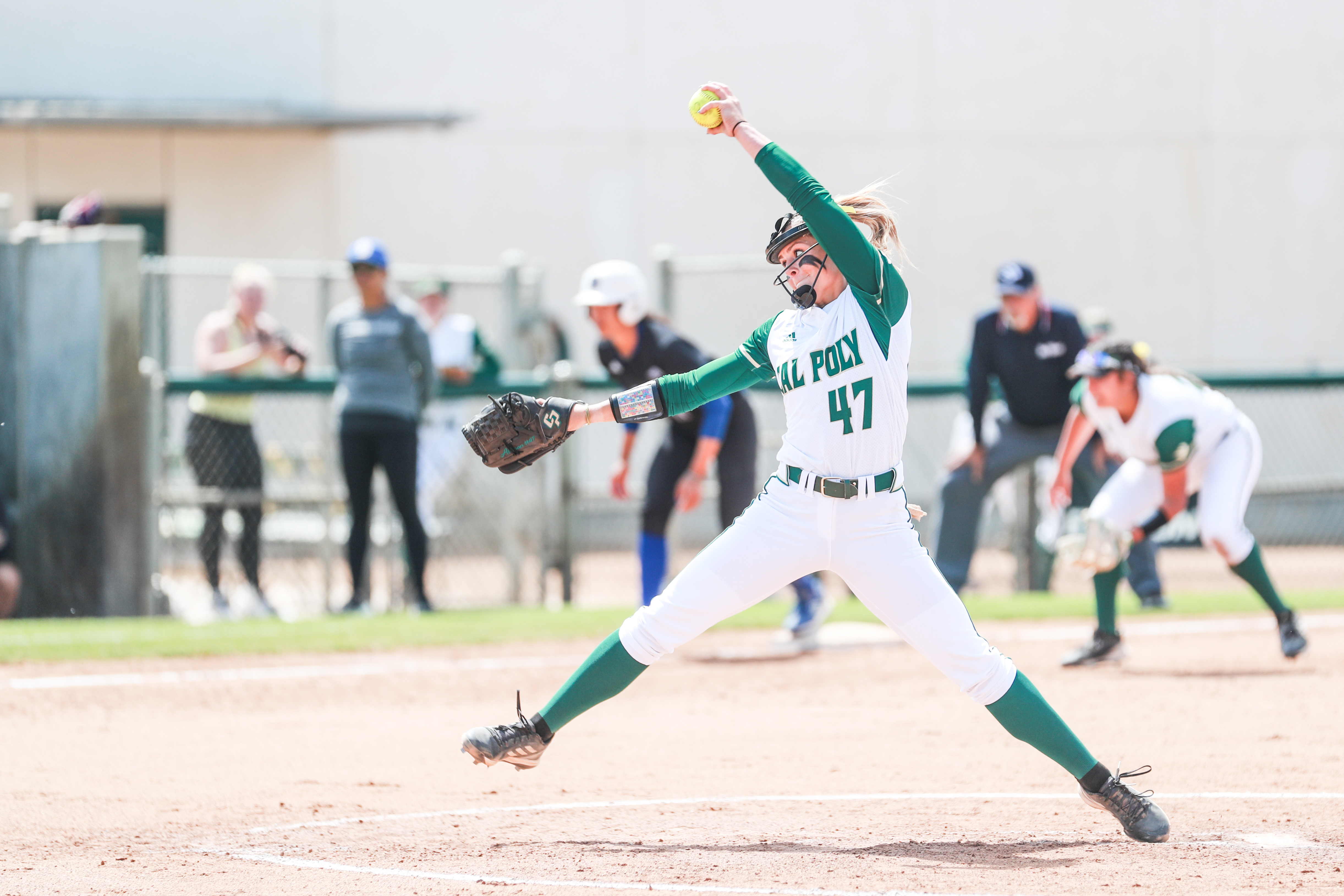 A woman wearing a Cal Poly softball uniform pitches a ball from the pitcher's mound.