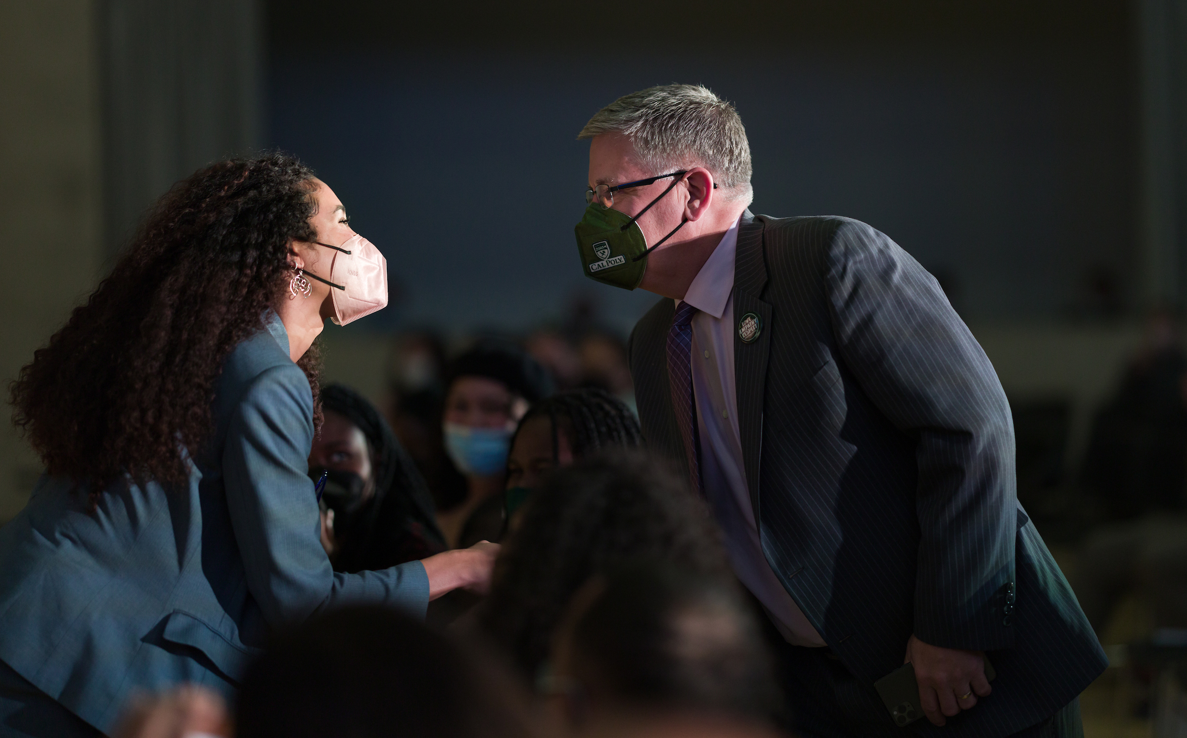 A woman wearing a suit and mask shakes hands with Cal Poly President Jeffrey Armstrong, also wearing a suit and mask. 