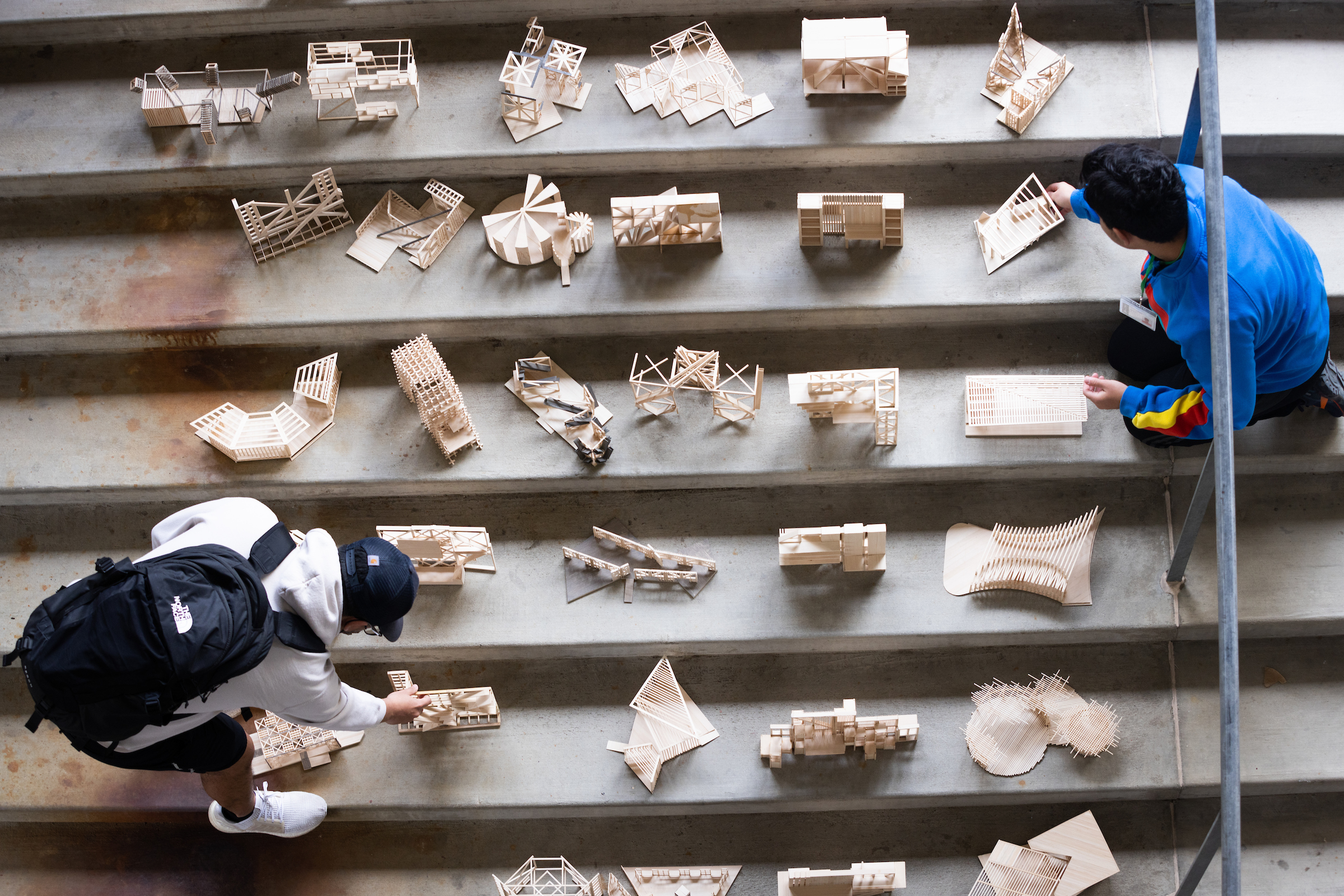 First-year architecture students with wooden models they created that rest on concrete steps.