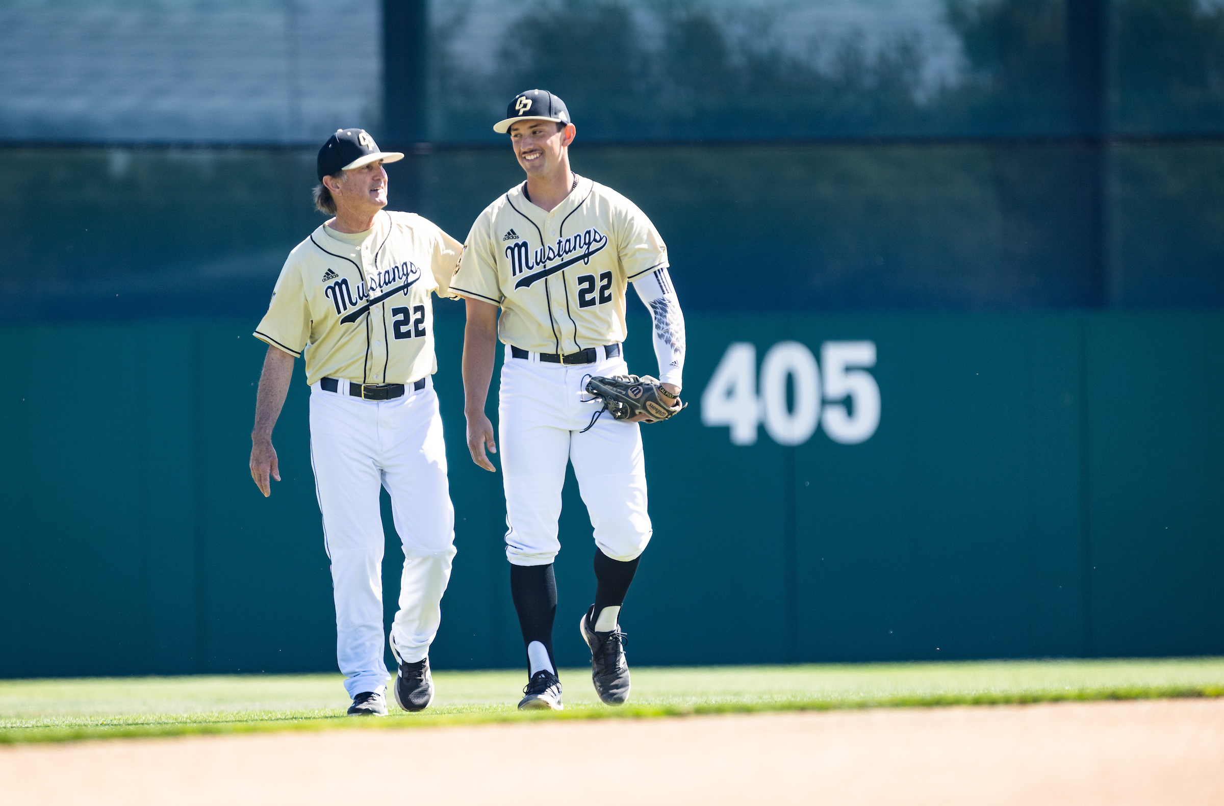 Cal Poly baseball player Brooks Lee and his dad, Larry Lee, wear their uniforms and walk together across the baseball diamond.