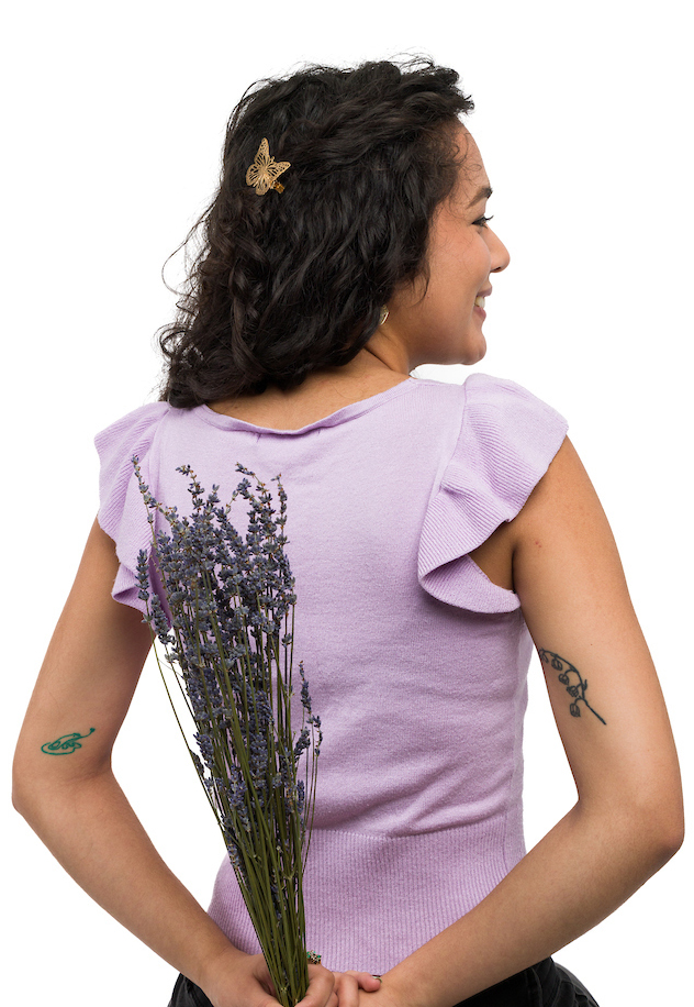 A young woman holds a bouquet of flowers behind her back while displaying arm tattoos of a frog and flowers