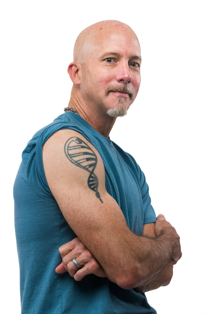 A man with a rolled up sleeve shows an arm tattoo of a black and white snake designed to look like a double helix
