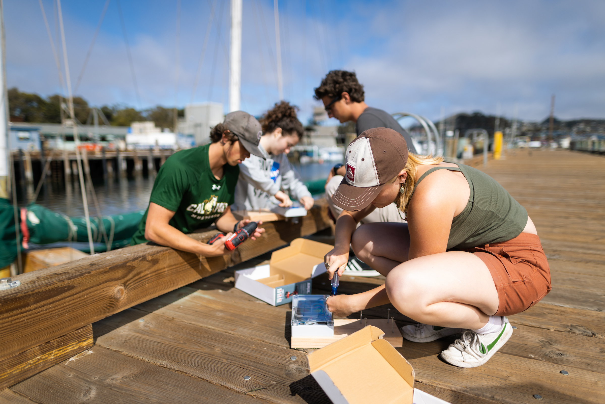 Students double check wave and tide sensors before installing them on the side of a wooden pier in Morro Bay.