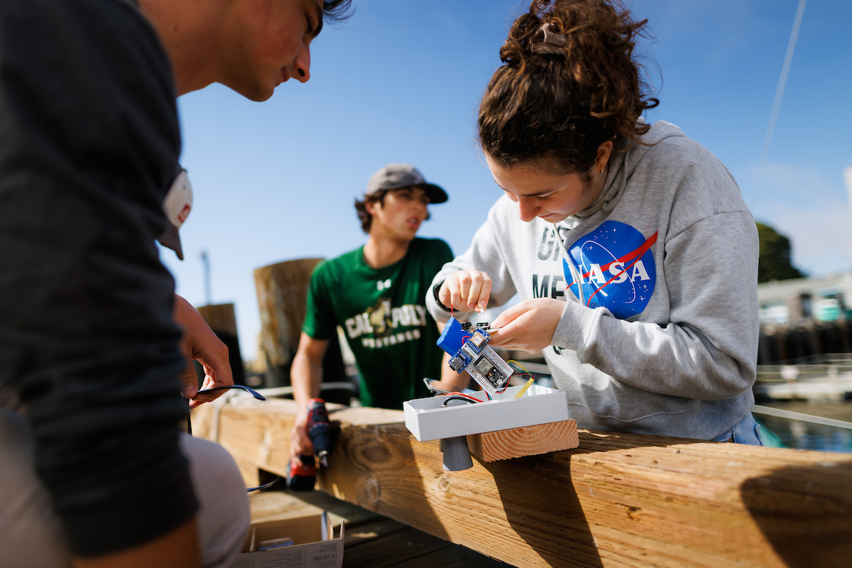 Three students work on a low cost wave and tide sensor at the coast guard pier in morro bay.