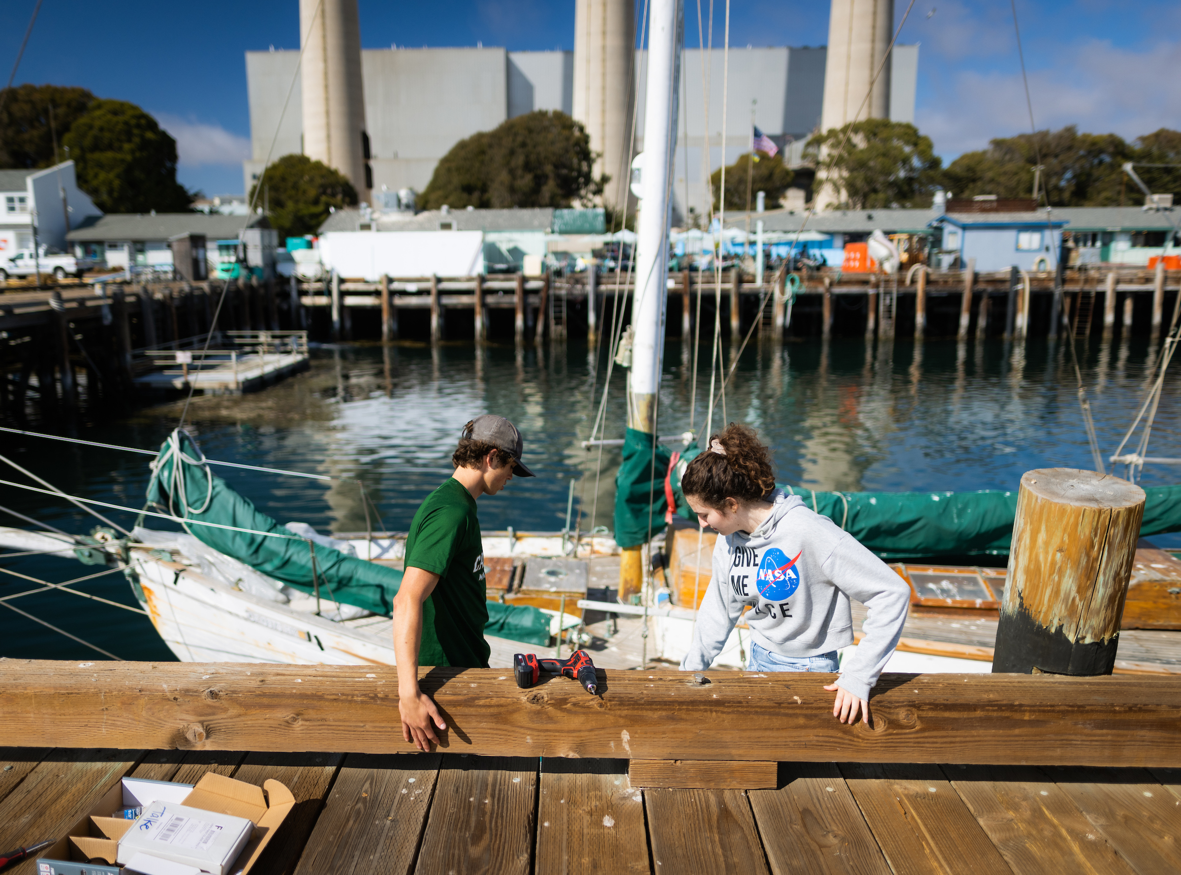 Two students hang off of a wooden pier as they check a scientific instrument.