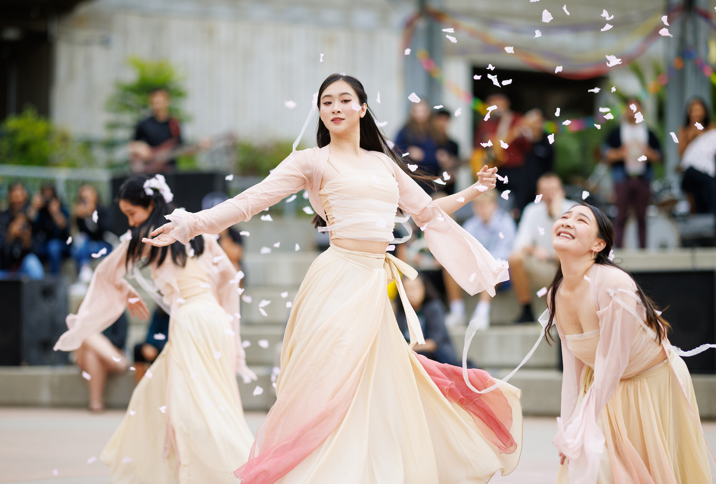 Students in light pink dresses perform a dance while flower petals float around them.