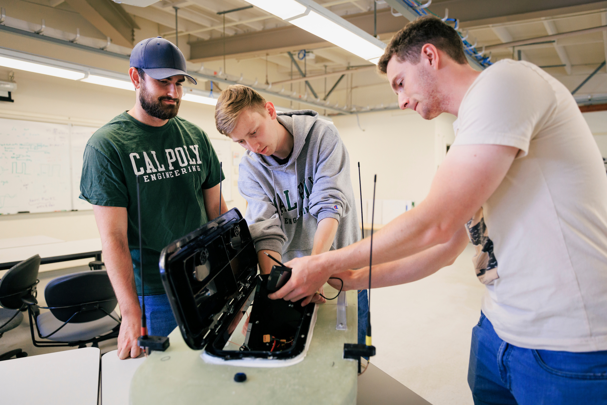 Three students work on the autonomous rescue vehicle, which looks like a small boat, in a lab at Cal Poly.