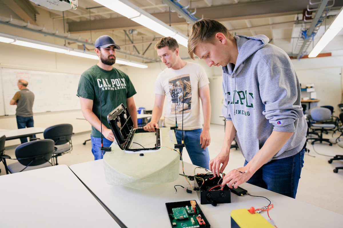 Three students work on the autonomous rescue vehicle, which looks like a small boat, in a lab at Cal Poly.