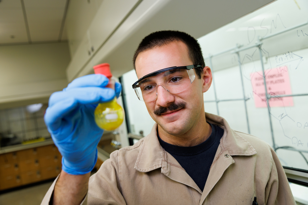Chemistry student Sal Deguara wears protective eye glasses and gloves as he holds up a potential compound for inspection.