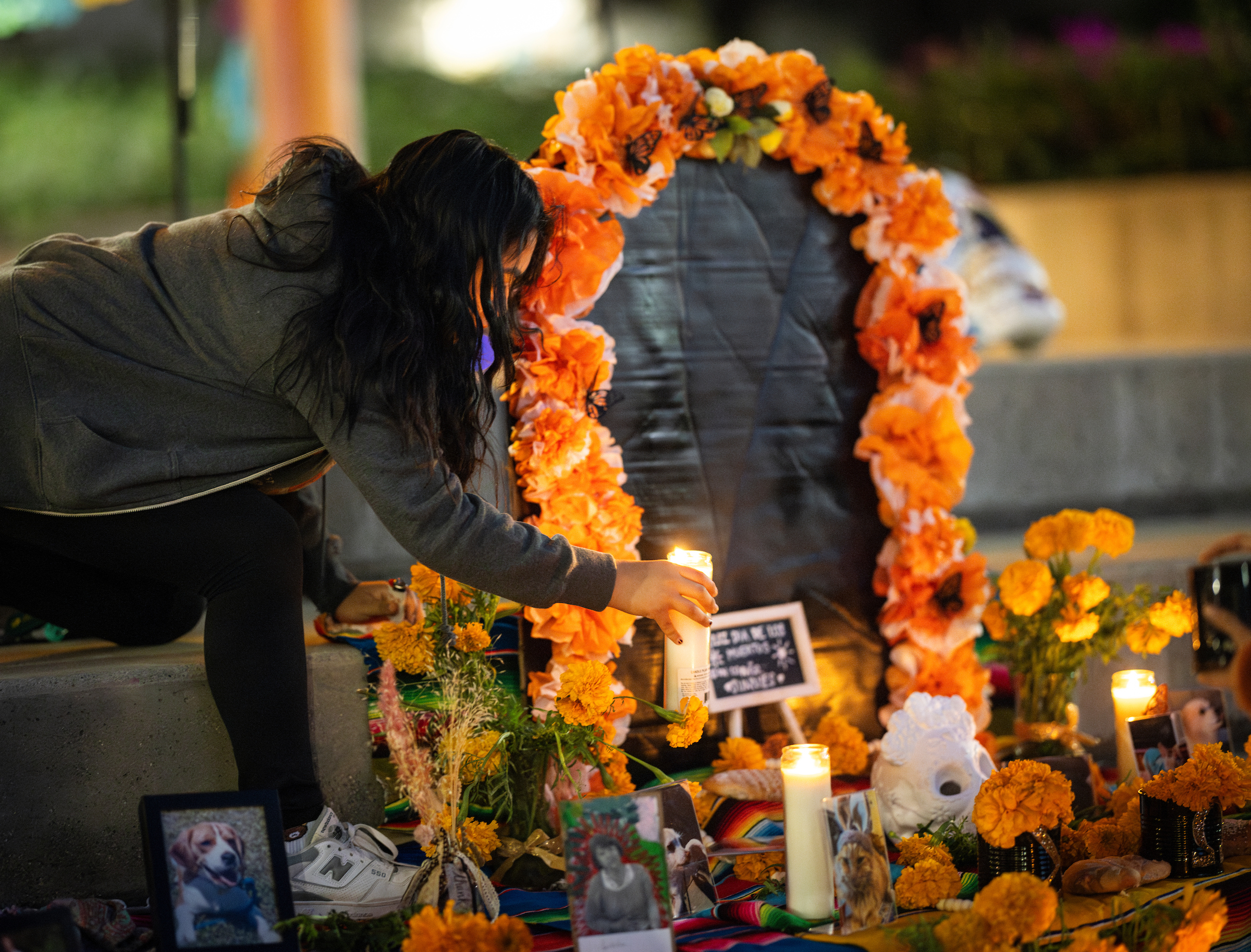 A student places a candle on an ofrenda, or altar, in UU plaza. 