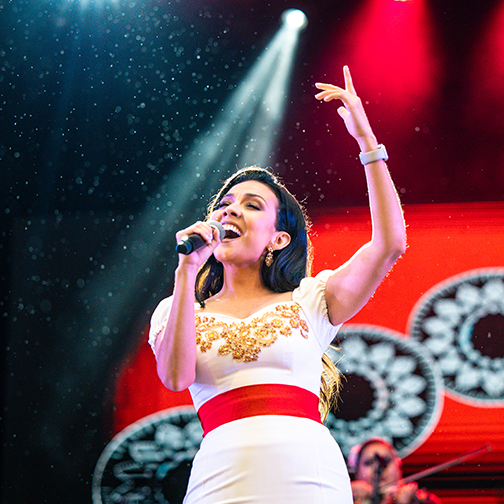 Lupita Infante singing on a stage with a white dress and red belt