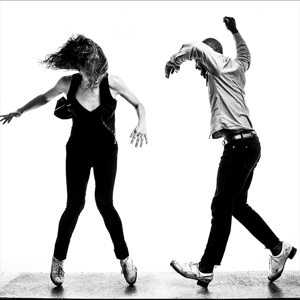 The black and white picture shows two people dancing on their toes, faces are not visible, but their clothing is wrinkled and flowing with their movement.