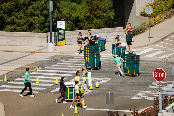 Students push green moving carts on the Cal Poly campus.