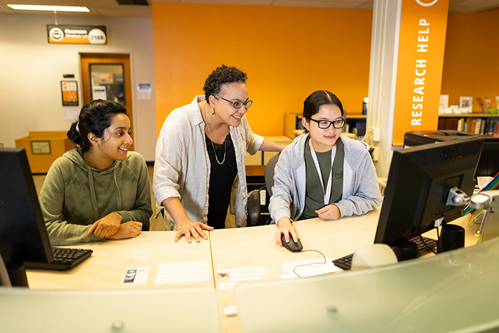 Farah Al-Nakib, Assistant Professor of History, works with students Suha Hussain, left, and Vi-Linn Vu at the Kennedy Library’s Research Help Desk