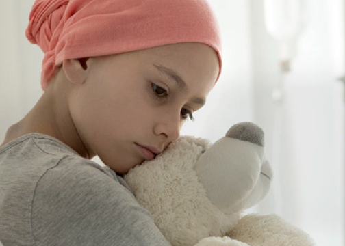 A young girl wearing a head covering hugs a teddy bear