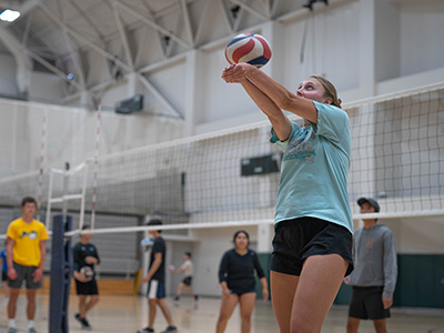 A woman plays volleyball with other team members in the background.