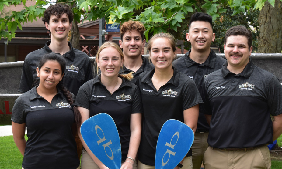 A group of students in black polo shirts holding canoe paddles