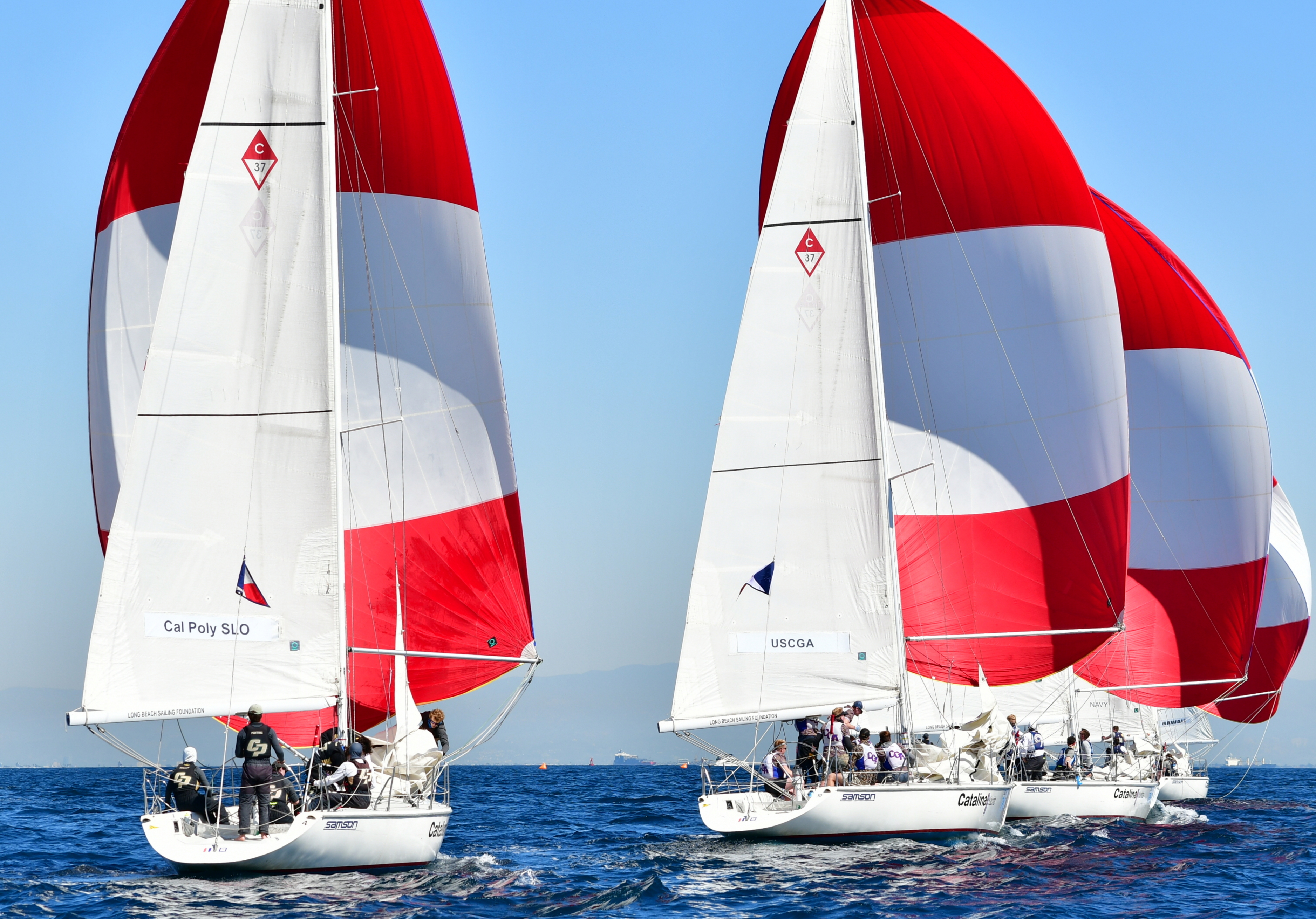 The Cal Poly Sailing Club's boat sailed next to the U.S. Coast Guard Academy's boat during a race on the ocean. Both boats are displaying red-and-white sails.