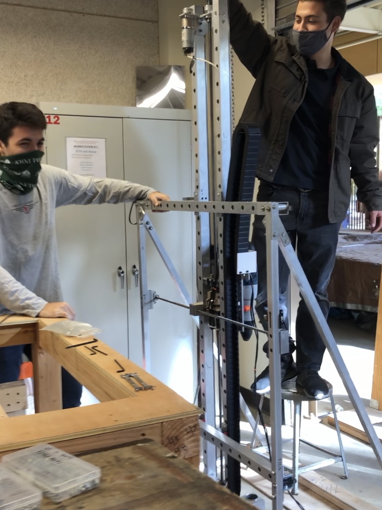 Two men wearing face masks work on a steel structure in the process of becoming a prototype developed by students. 