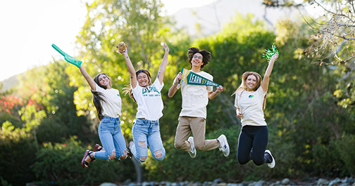 Four students with Cal Poly shirts or spirit wear jump in the air.
