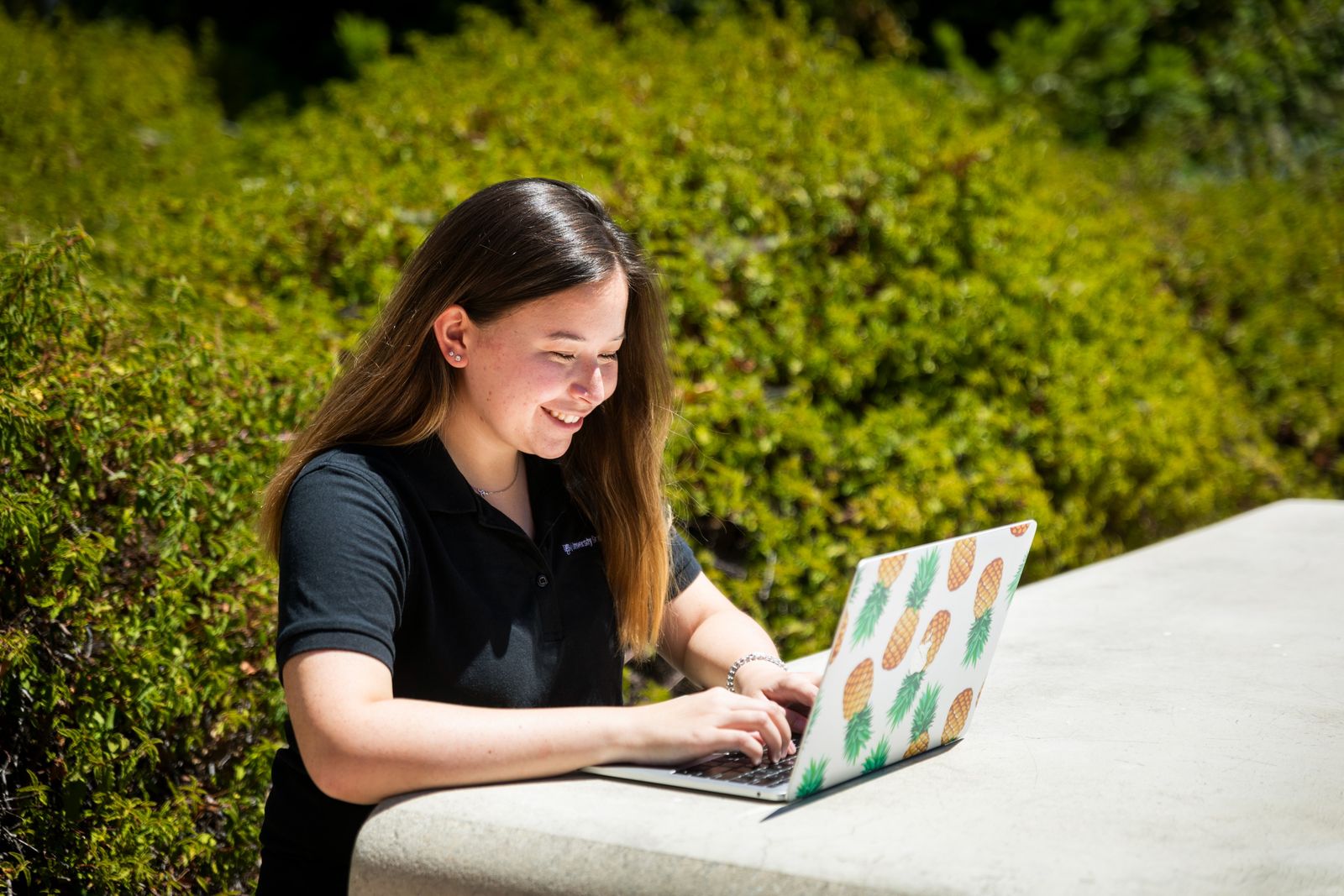 Student sits at a table outside working on a laptop