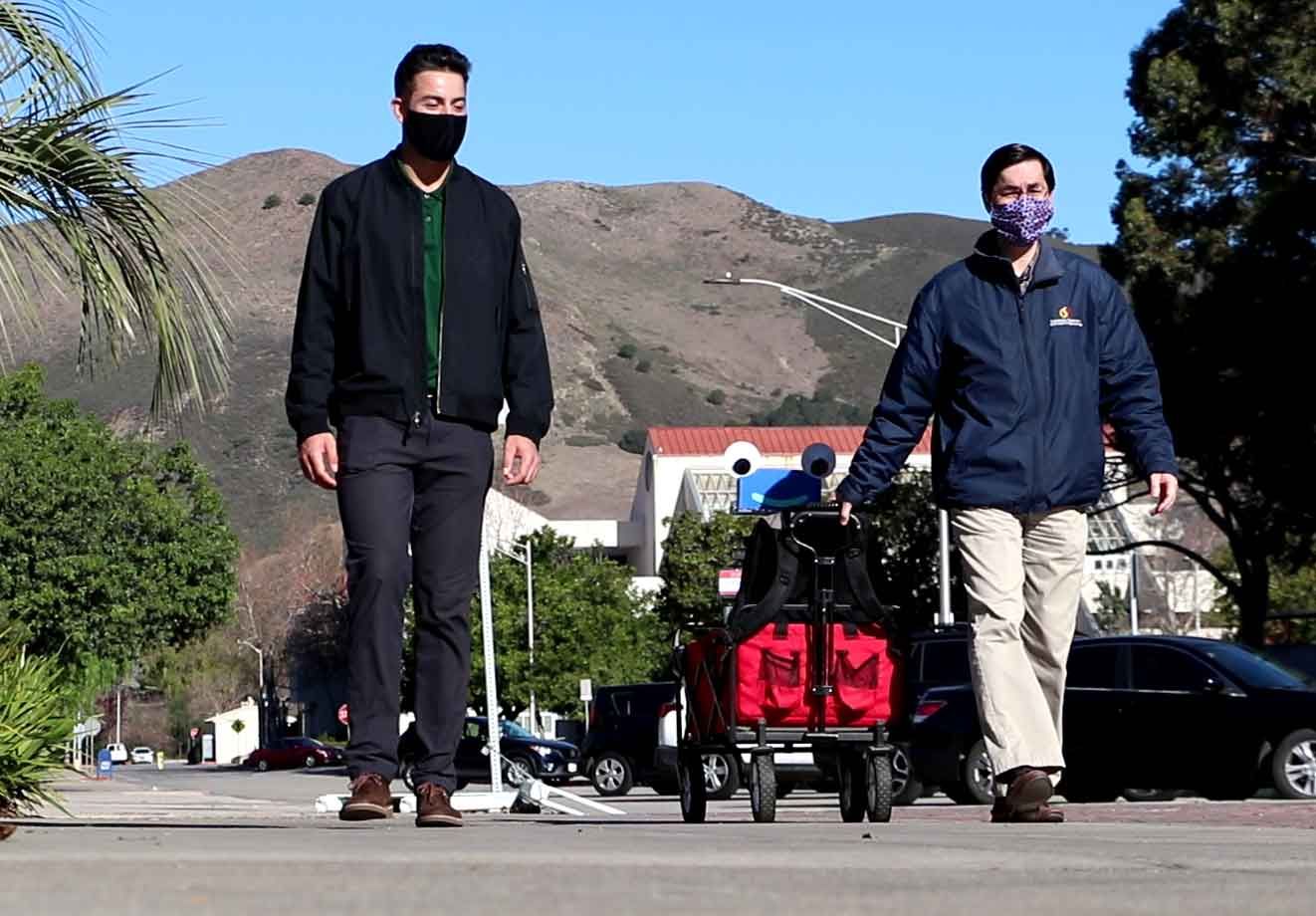 John Seng walks with former student Daniel Jones and Herbie, a robot Seng created.