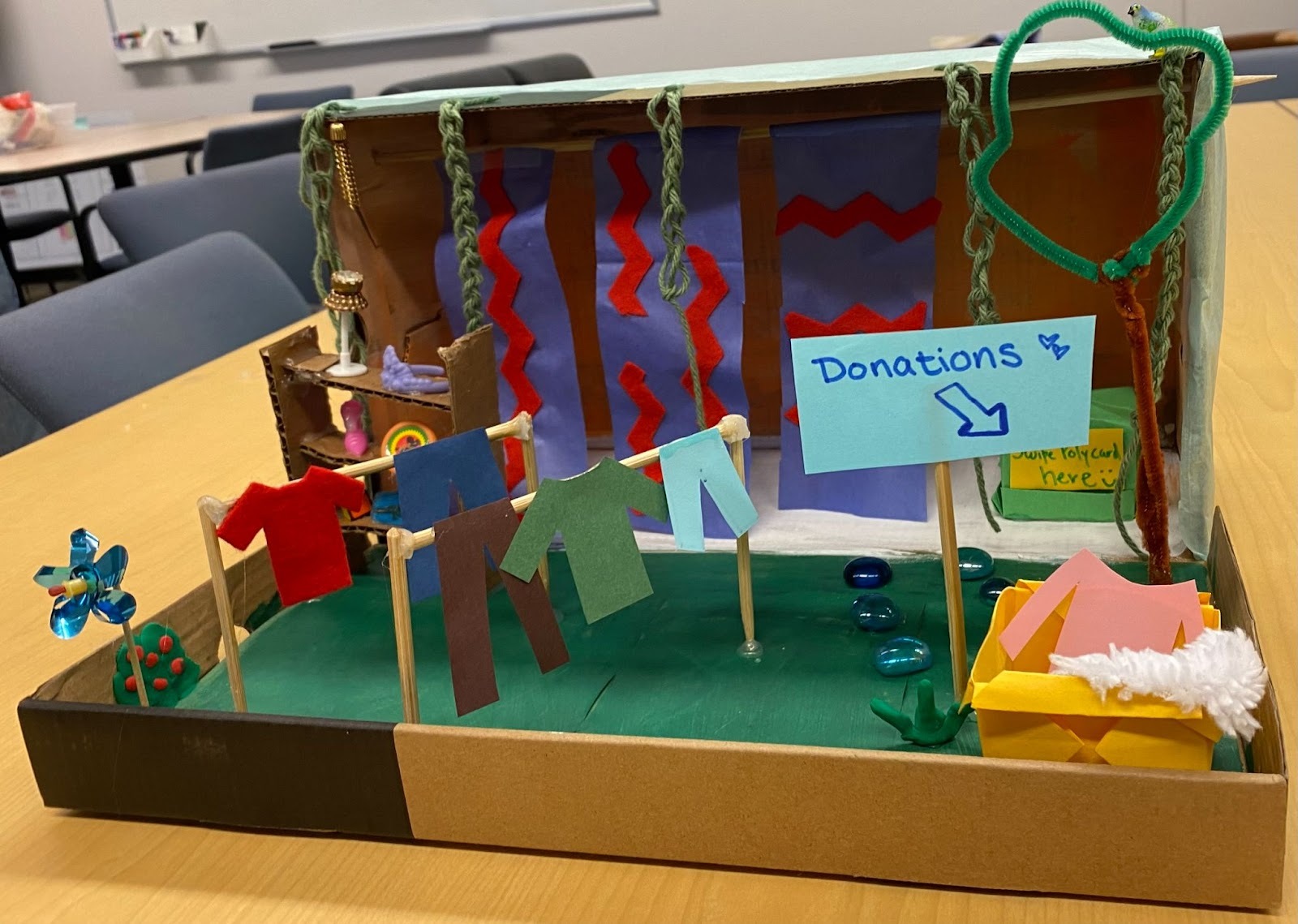 A diorama of a clothing swap showing clothes, a donation box and decorations. 