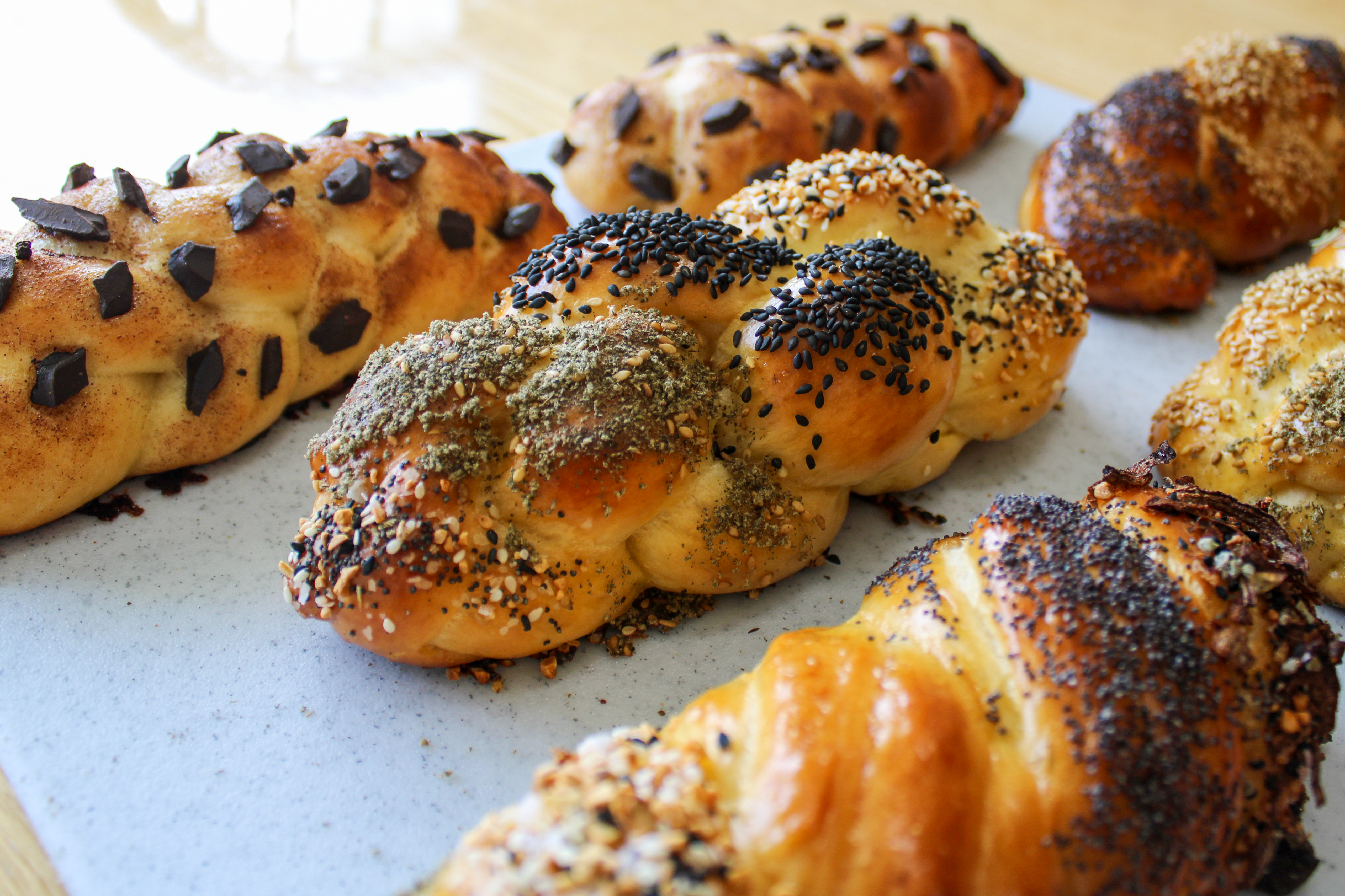 Loaves of challah, a braided bread, lay next to each other. Each loaf has different toppings.