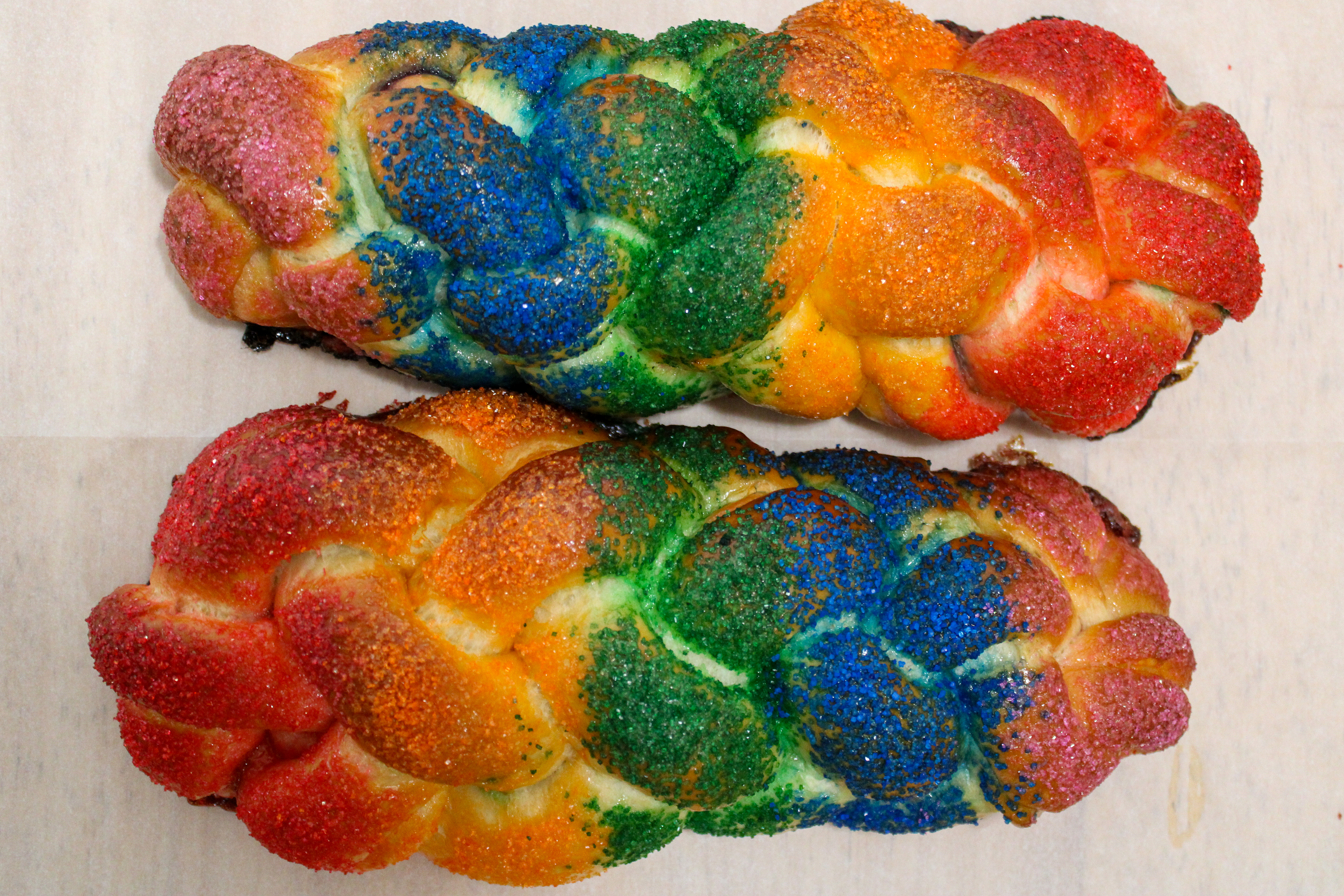Two loaves of challah, a braided bread, are covered in sparkly rainbow topping.