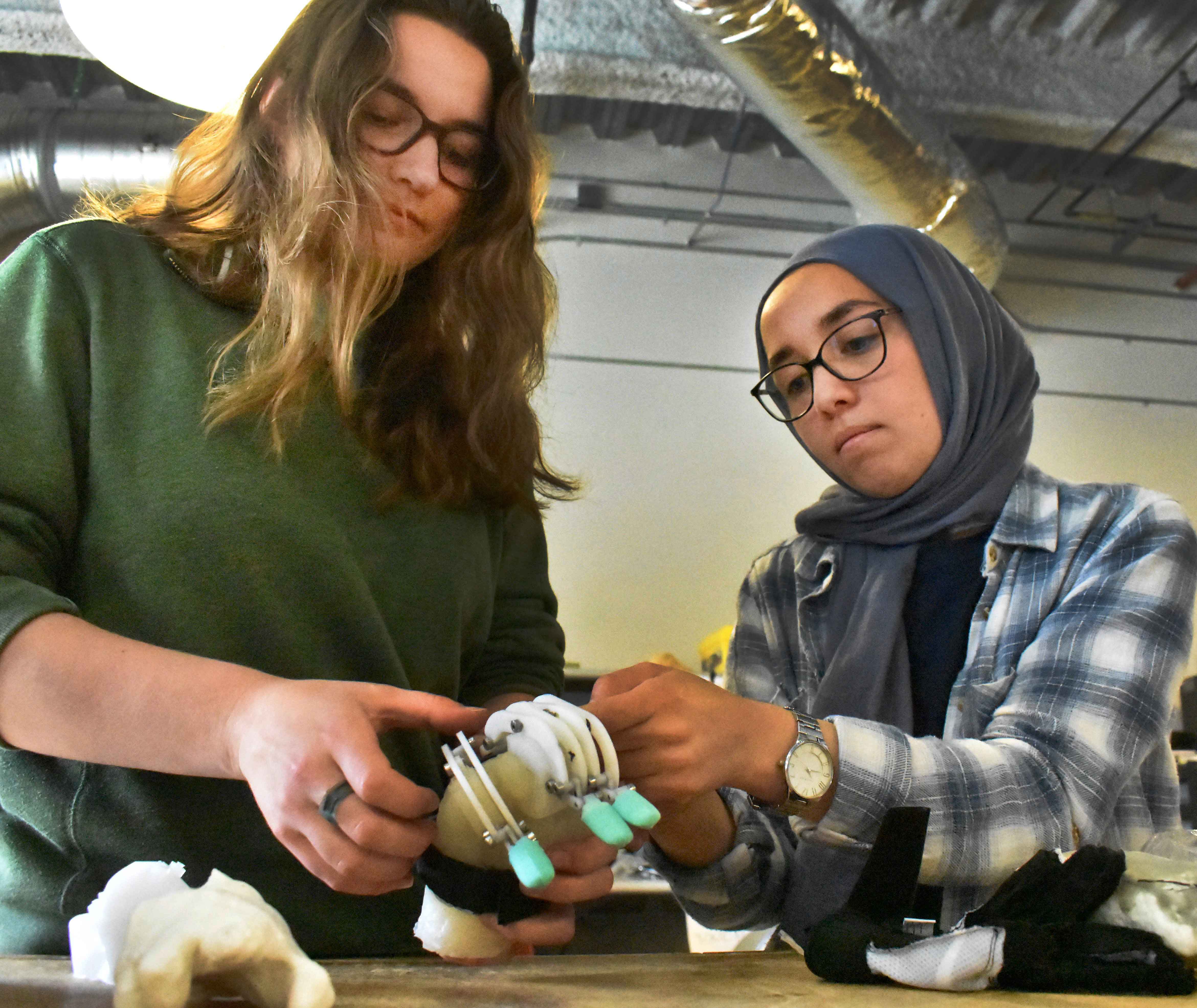 Students Janis Iourovitski and Leila Assal arrange a set of mechanical fingers on a rubber mold of Julian's right hand in a Cal Poly classroom. 