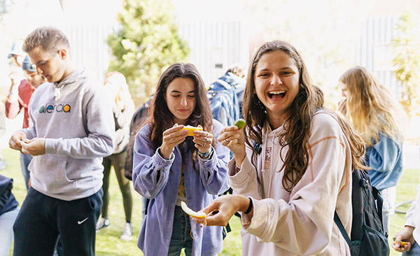Two students smile as they eat wedges of lime and lemon during a taste test party outside on campus.